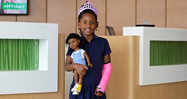 Young girl in a crown smiling with a broken arm in a pink cast.