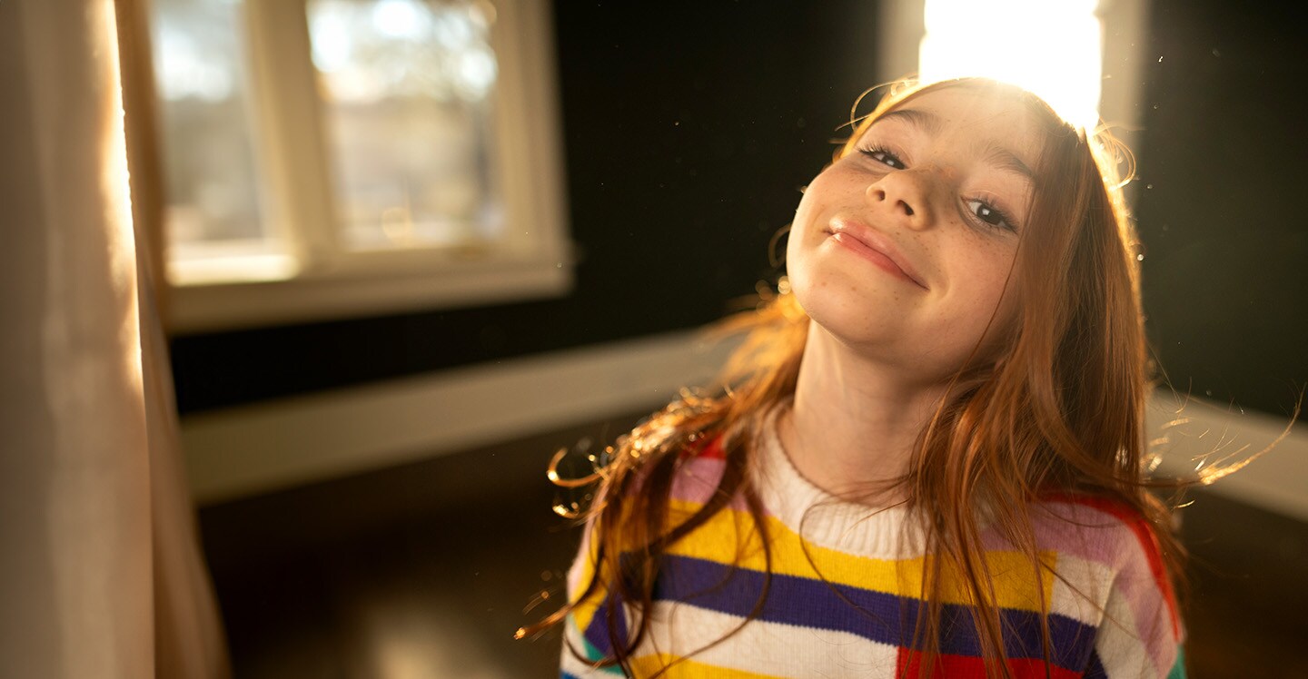 Young girl in striped shirt smiles in sunny room.