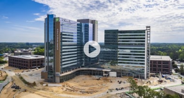 new pediatric hospital with landscaping and roadways under construction, with a play button