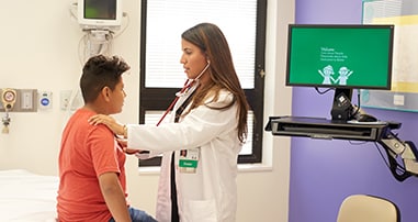 Doctor listening to stethoscope with a young boy at an urgent care