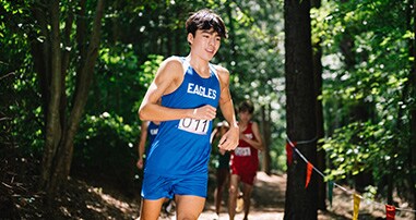 Teen male cross country runner during race through the woods.