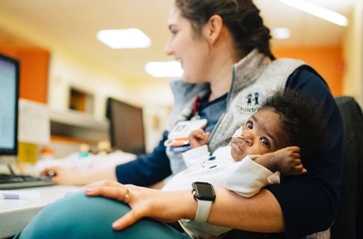 pediatric nurse cradles infant patient at nurse's station