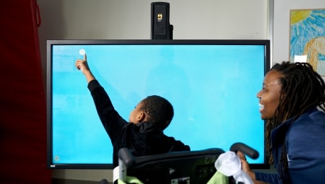 A child touches a computer screen while receiving technology assisted therapy 