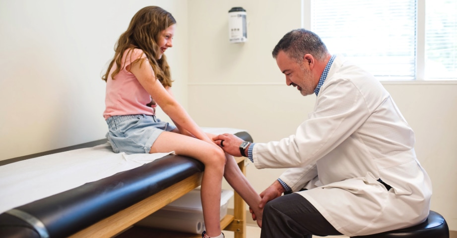 Orthopedic surgeon examines child’s ankle on exam table  
