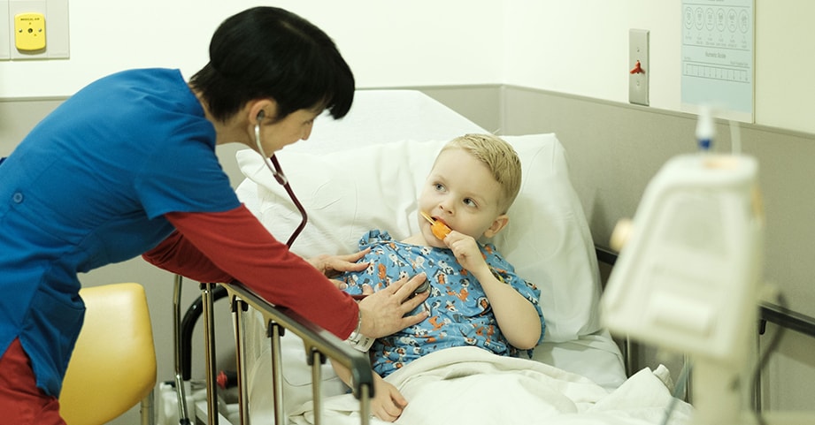 A nurse gives a little boy an orange  popsicle after surgery.