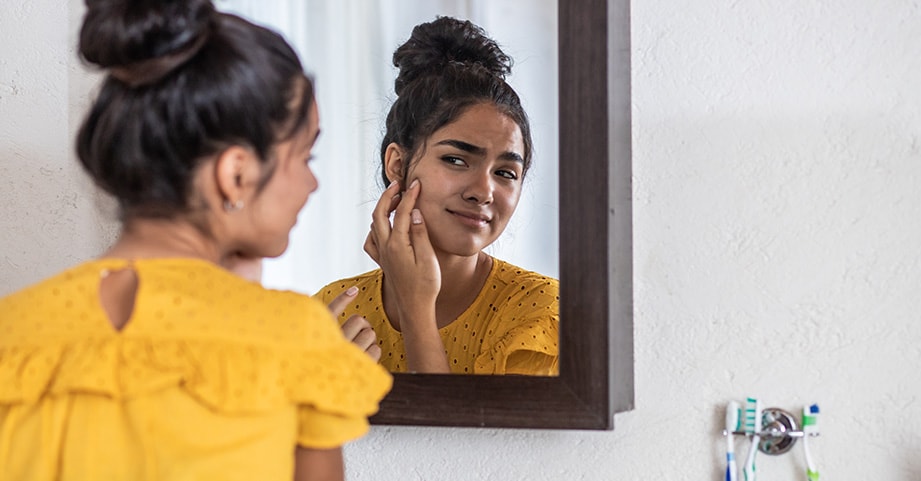 Teenage girl looking at her face in mirror