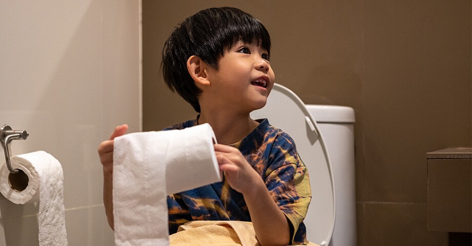 Toddler boy sitting on potty holding roll of toilet paper