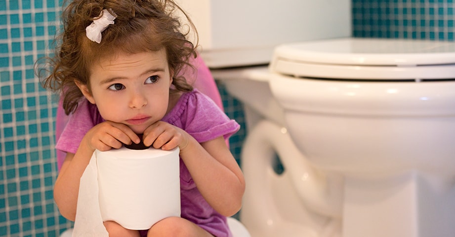 Toddler girl sitting in bathroom holding roll of toilet paper