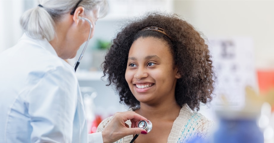Doctor uses stethoscope to listen to a teen patient's heart. 