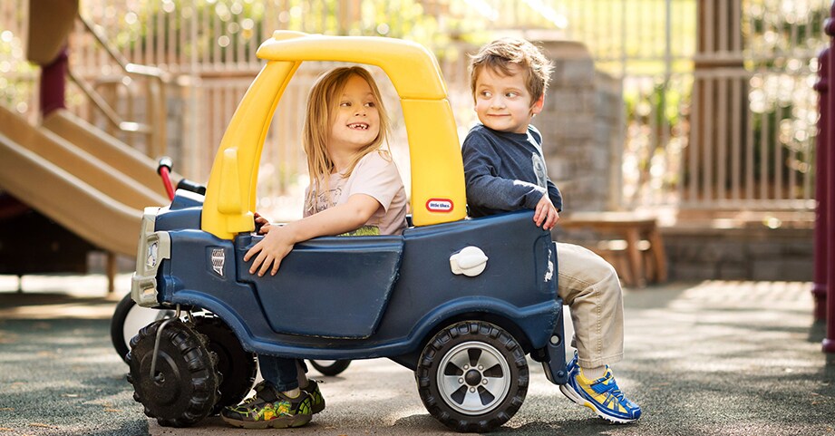 Boy and girl riding in car on playground at preschool