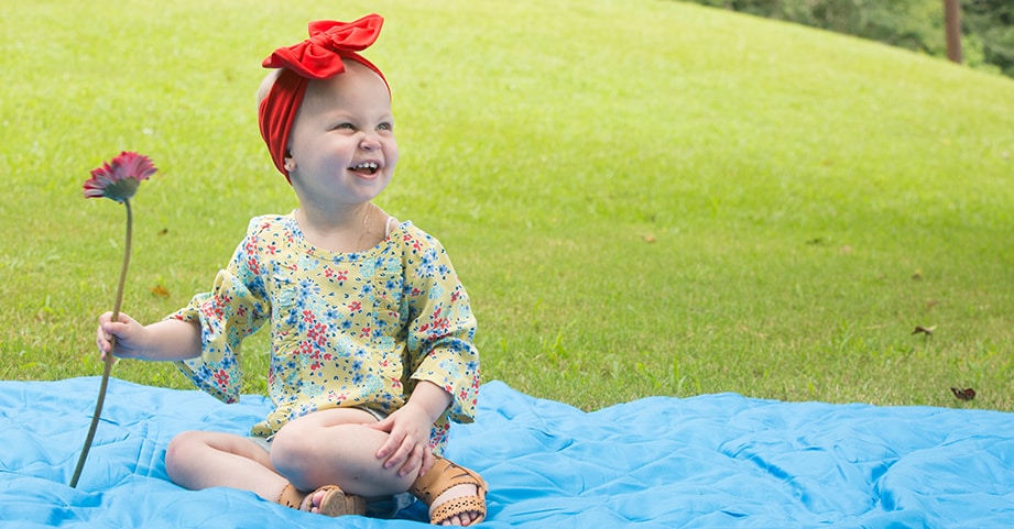 Girl with pediatric cancer smiling with flower in hand