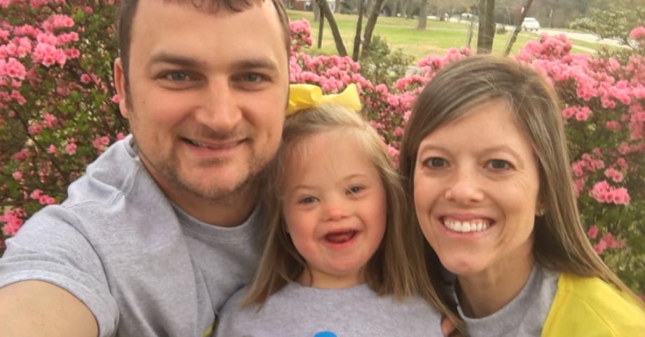 young girl with down syndrome smiling with her parents in matching t-shirts