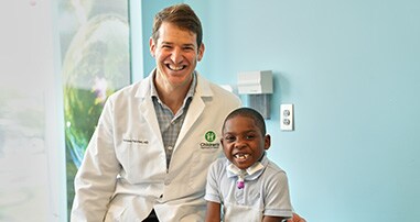 Pediatric orthopedic doctor smiling and posing with a patient boy sitting on check-up table at a spine appointment