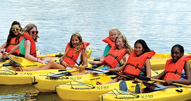 Teen girls smiling in kayaks at Camp Courage