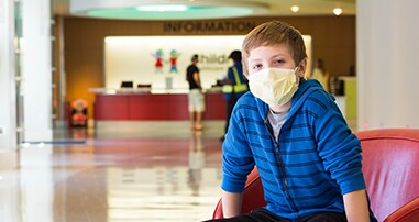 Boy wearing facemask sitting in chair in Egleston lobby