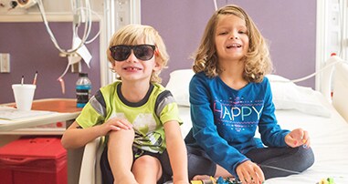 Brother and sister smiling and sitting on a bed in pediatric hospital