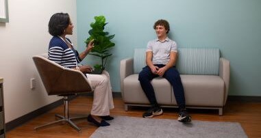 teen sitting on a couch speaking to a pediatric psychologist who is sitting in a chair