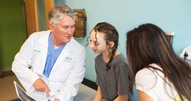 Pediatric spine surgeon, Dr. Bruce, discusses spine surgeries with female patient and her parent in a clinic room.