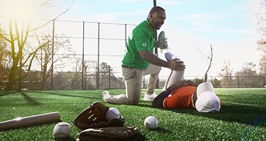Children's athletic trainer on field helping teen baseball player stretch before a game.