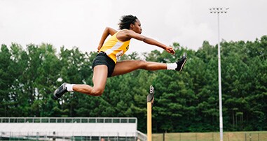 Female teen athlete jumps over hurdles on high school track.