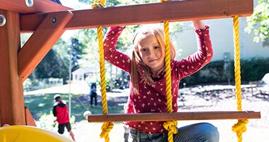 An elementary school-aged girl climbing a rope ladder on a playground. 