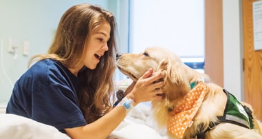 girl in hospital bed playing with therapy dog
