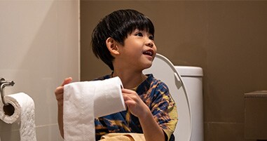 Little boy sitting on toilet holding toilet paper
