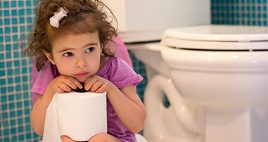 Toddler girl sitting on potty holding roll of toilet paper