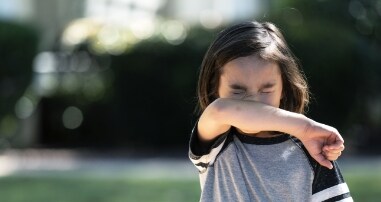 Young child coughing into elbow