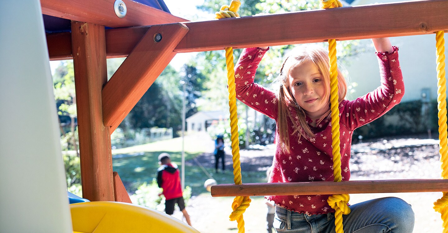 An elementary school-aged girl climbing a rope ladder on a playground. 