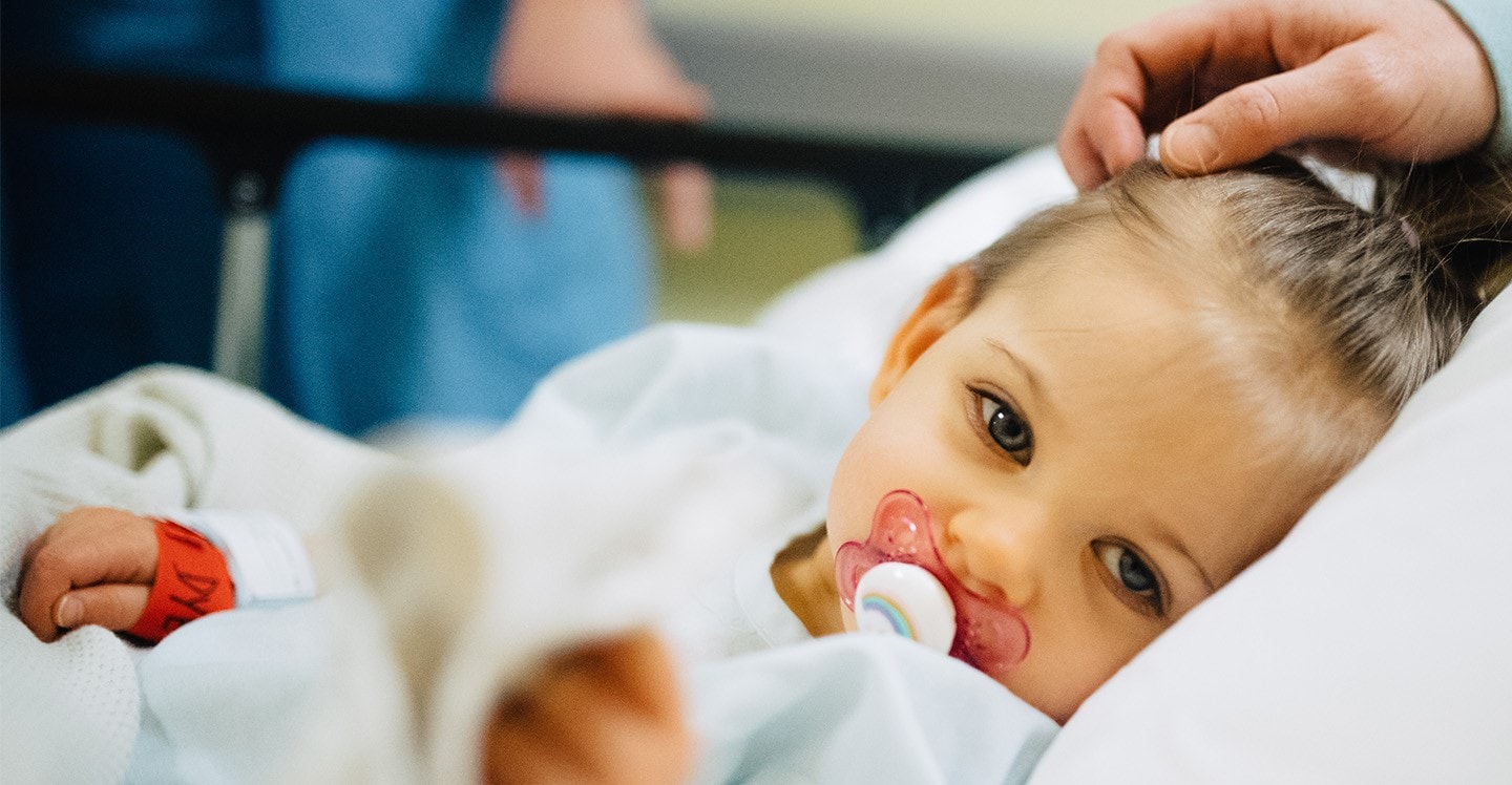 little patient girl looking at the camera with a pacifier in her mouth in a pediatric hospital bed