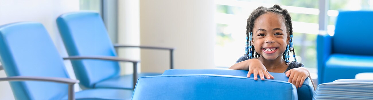 Toddler girl peeking over chairs in clinic