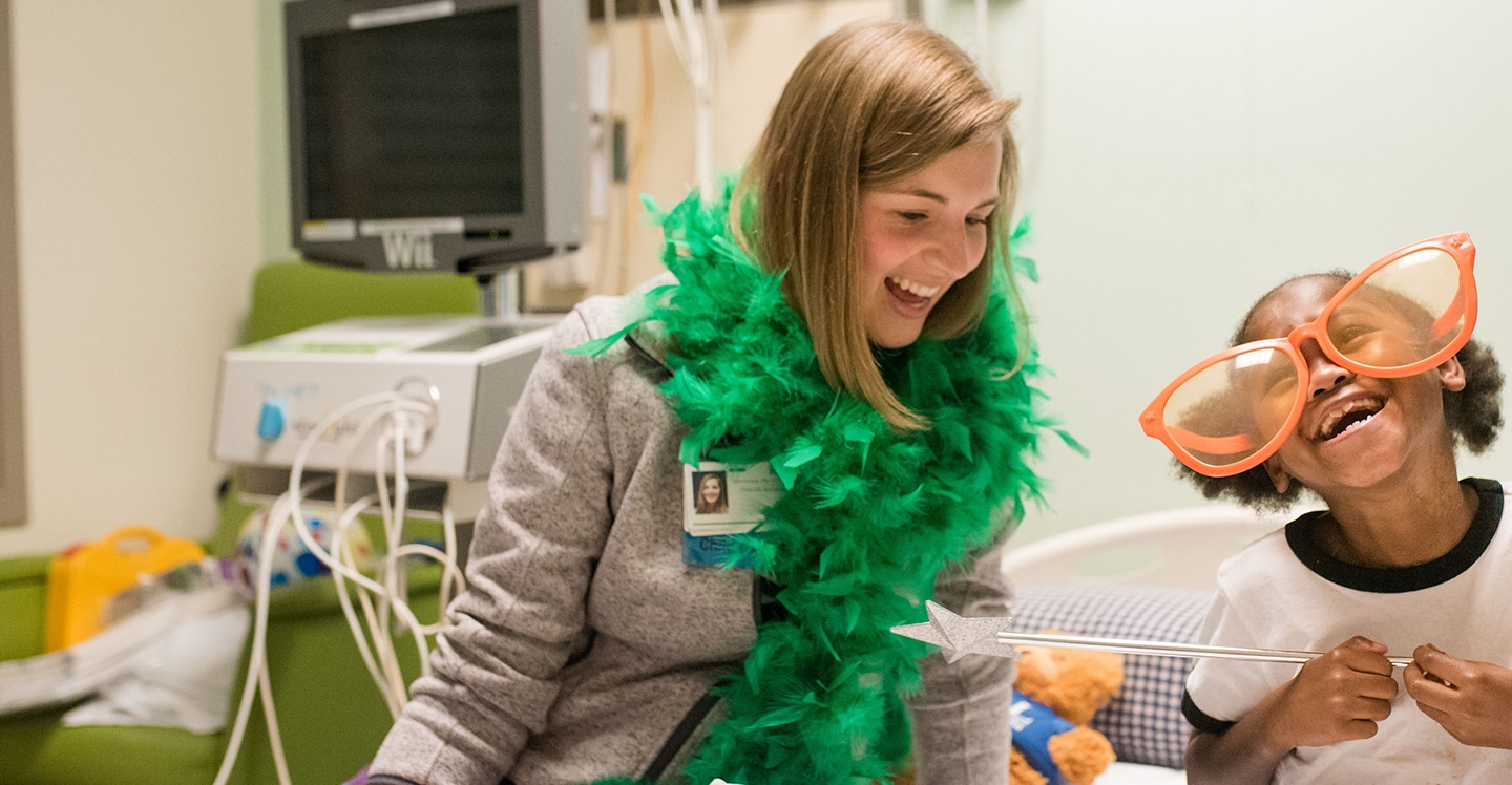 Patient girl and child life specialist playing dress-up in pediatric hospital room