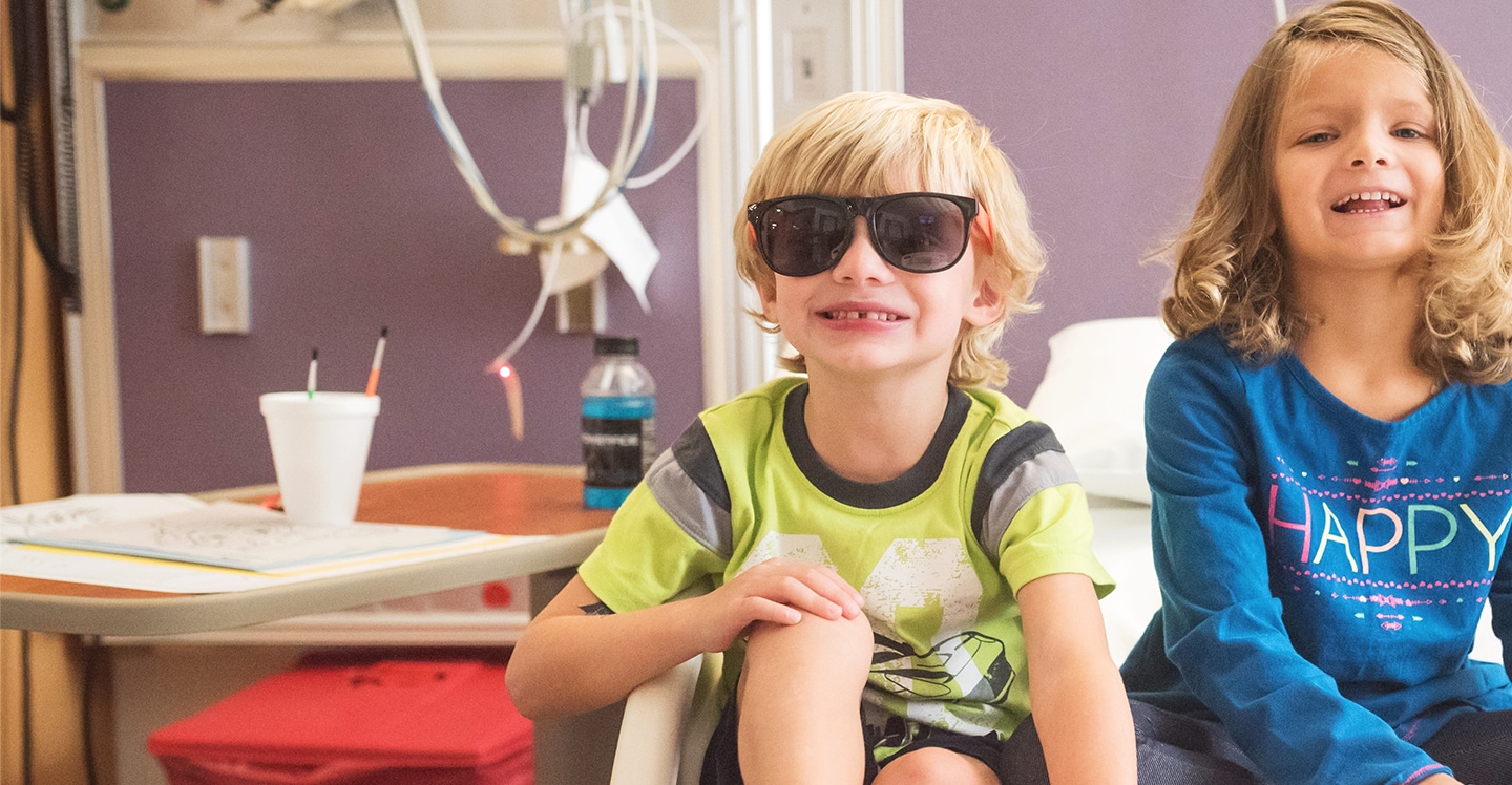 Brother and sister smiling and sitting on a bed in pediatric hospital