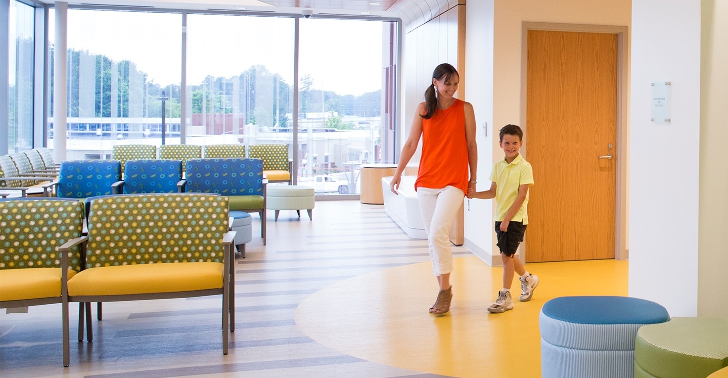 Young boy walking with mom into children's waiting room at town center outpatient care center