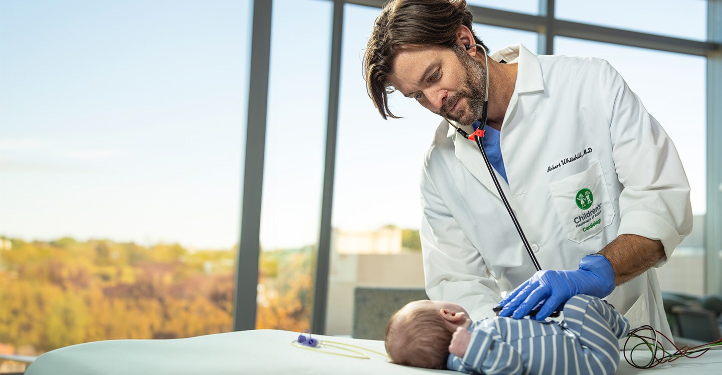 A cardiologist listens to an infant's heart in a hospital bed.