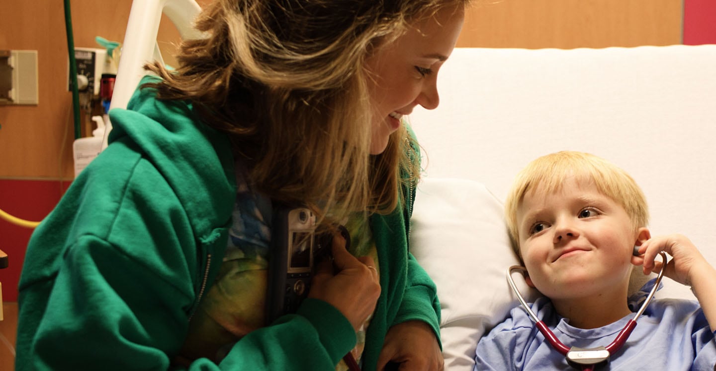 nurse with child in hospital bed playing with stethoscope