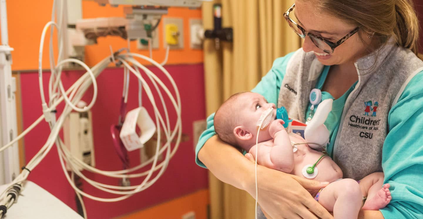 nurse holding baby over crib in hospital room