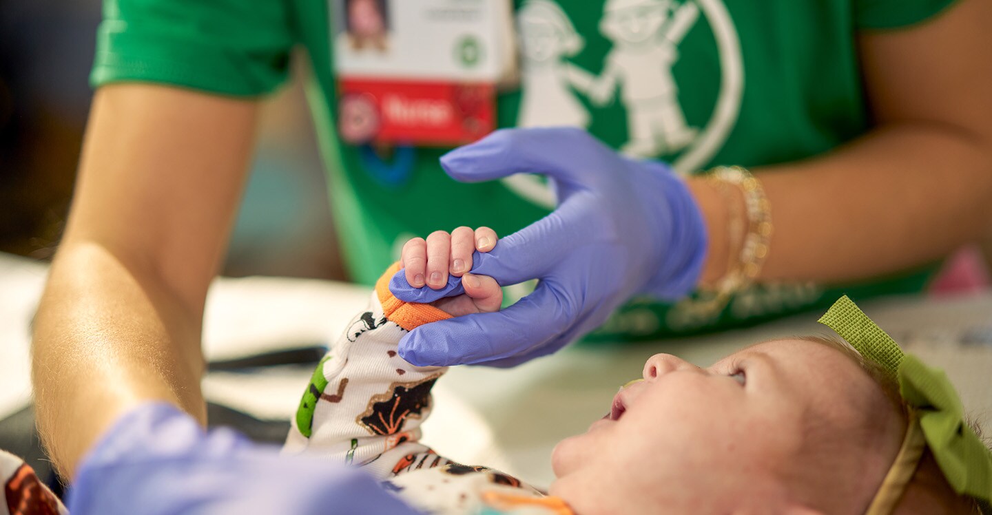 Infant in the Cardiac Acute Care Unit holds a cardiac nurse's finger and laughs 