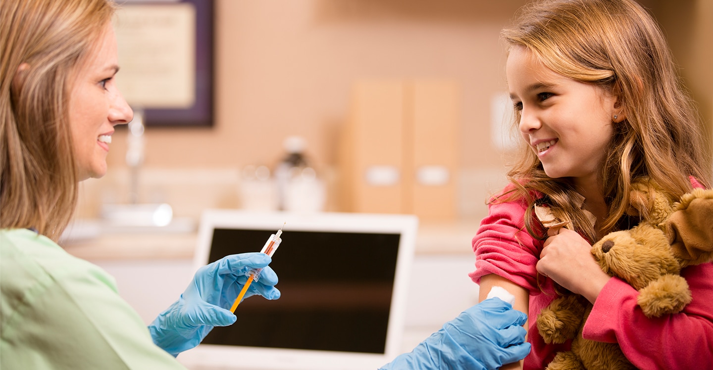 young girl holding teddy bear while getting flu shot