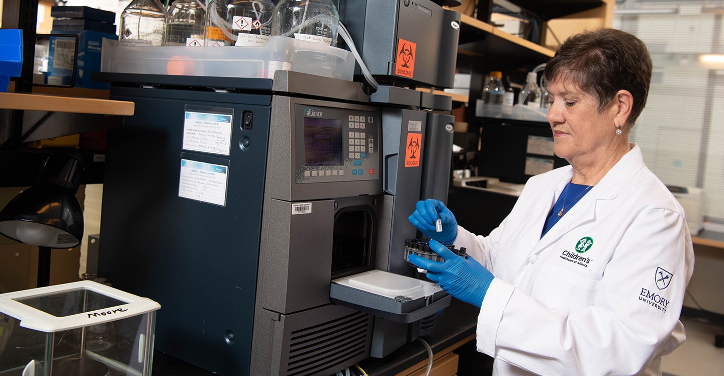 Children’s and Emory researcher wearing lab coat examining vial in laboratory