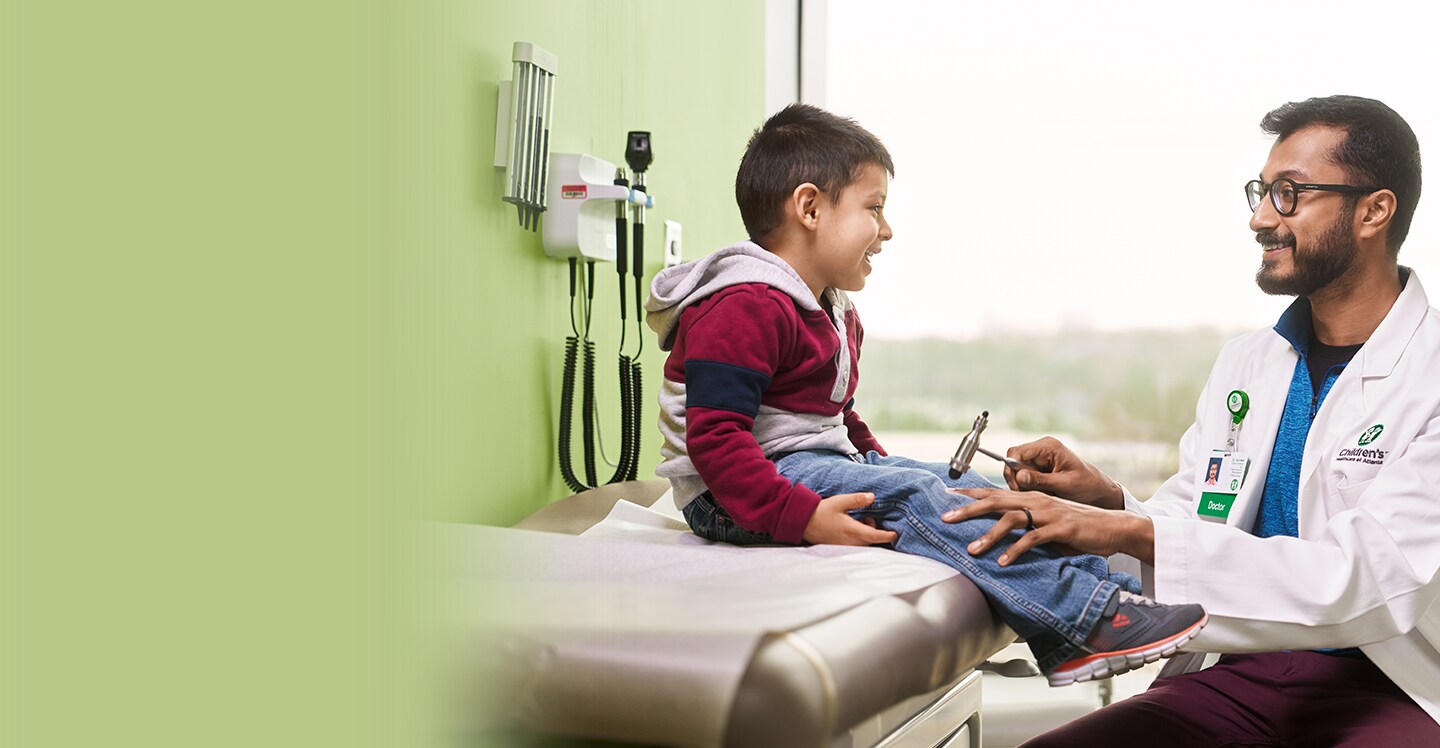 Pediatric neurologist testing reflexes of young patient boy at clinic appointment