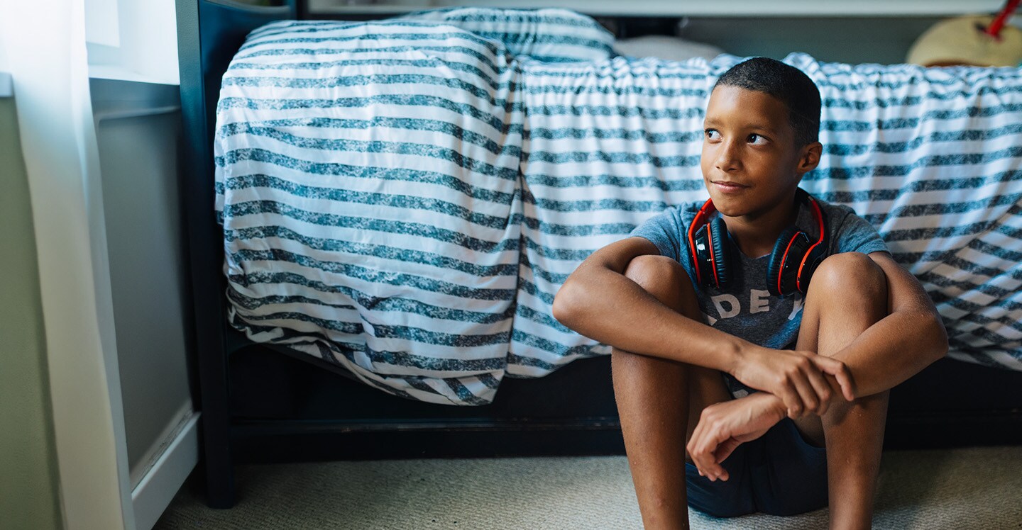 Child with headphones sitting on bedroom floor and smiling.