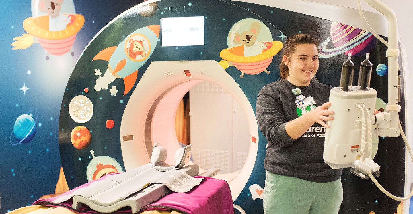 Healthcare provider standing in front of CT scan machine decorated with planets and spaceships.