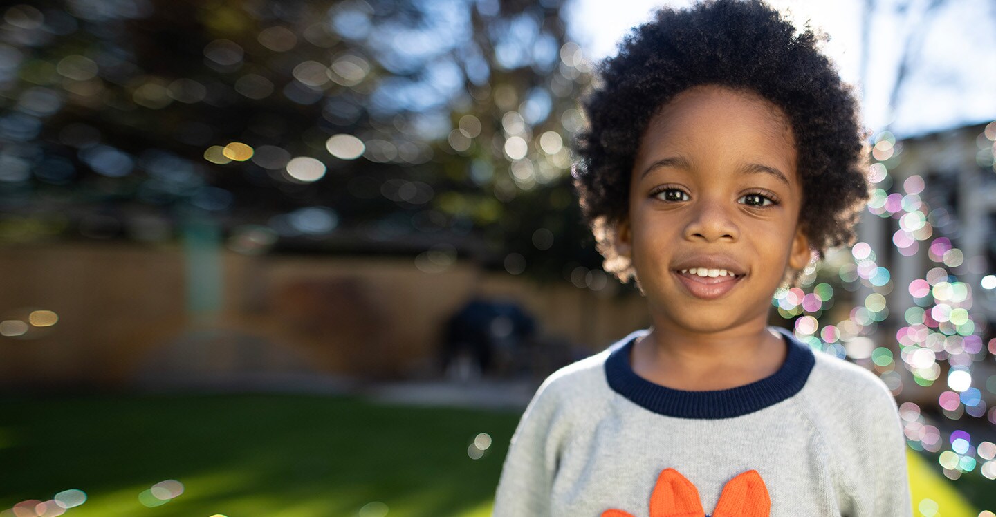 Boy smiling outside in sunshine with bubbles in the background.