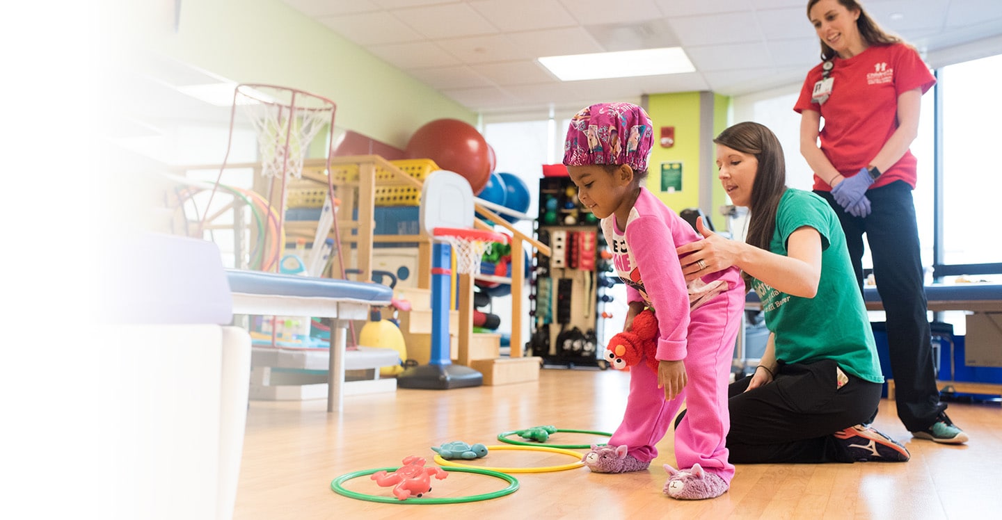 Little girl picks up rings in rehabilitation with nurse