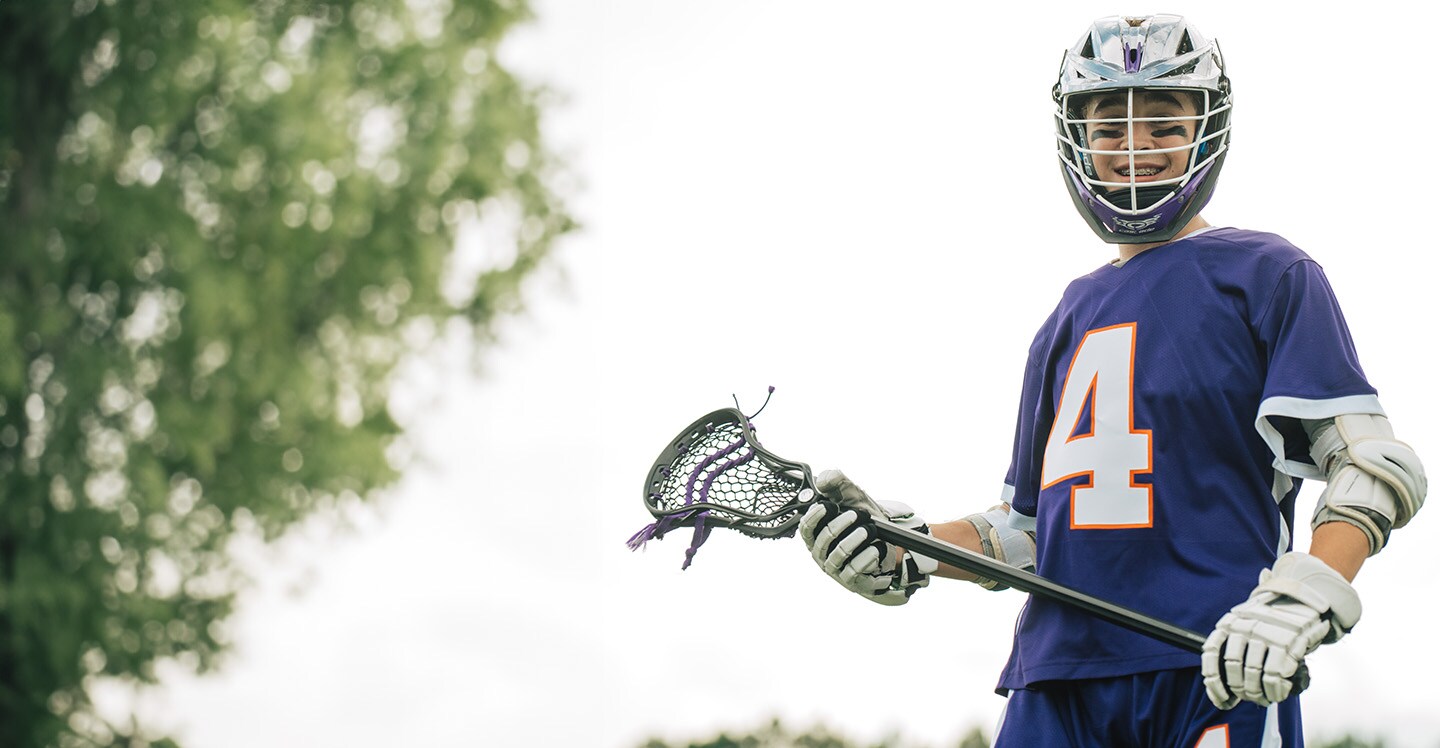 Teen male lacrosse player on field holding lacrosse stick.