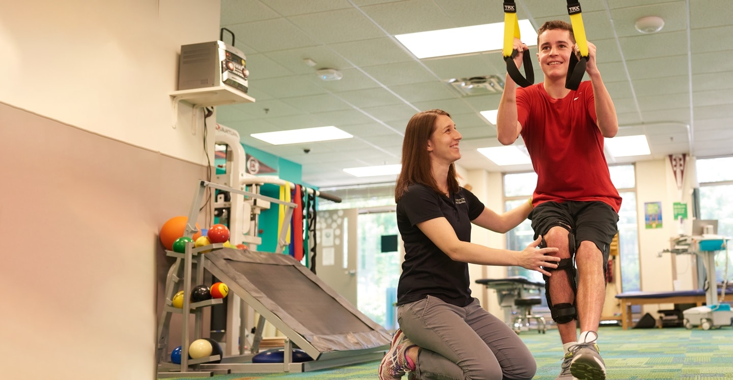 Pediatric sports physical therapist guiding teenage athlete after knee surgery