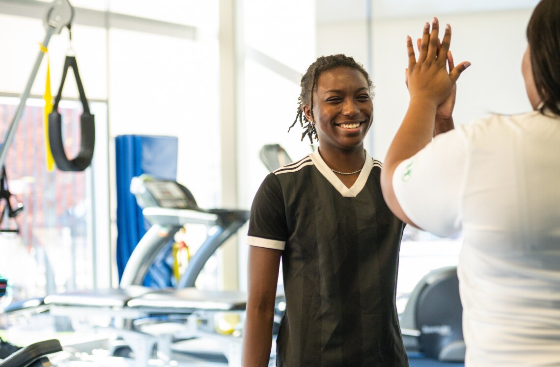 Pediatric sports physical therapist high fives smiling teen in sports physical therapy gym