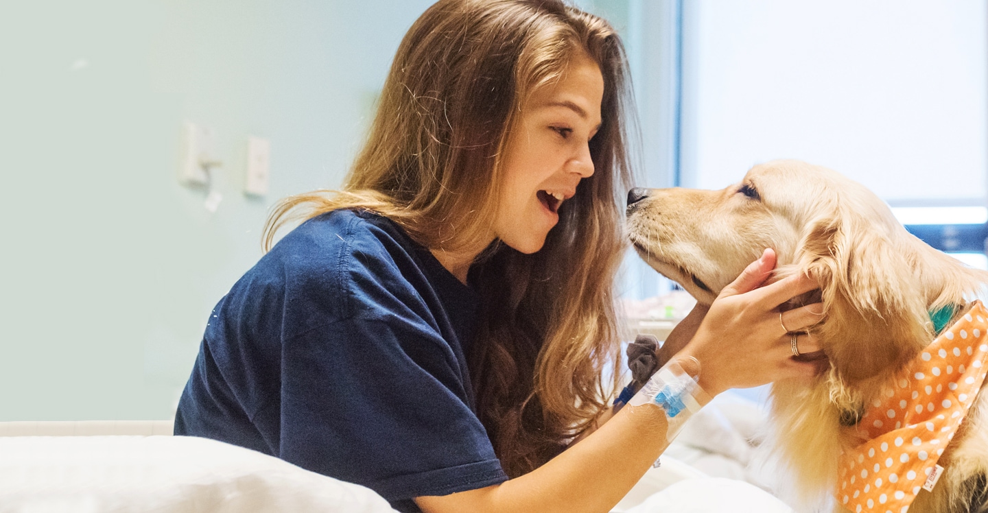 girl playing with therapy dog in hospital bed
